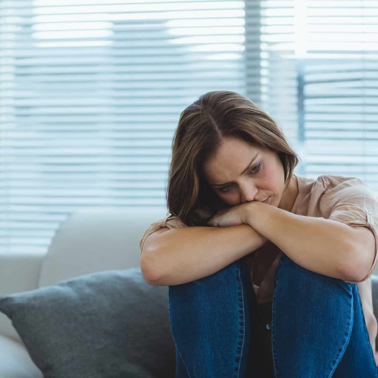 Sad young woman sitting on sofa at home